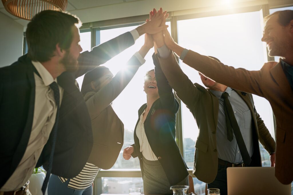 A group of business professionals celebrating team success with a high-five.