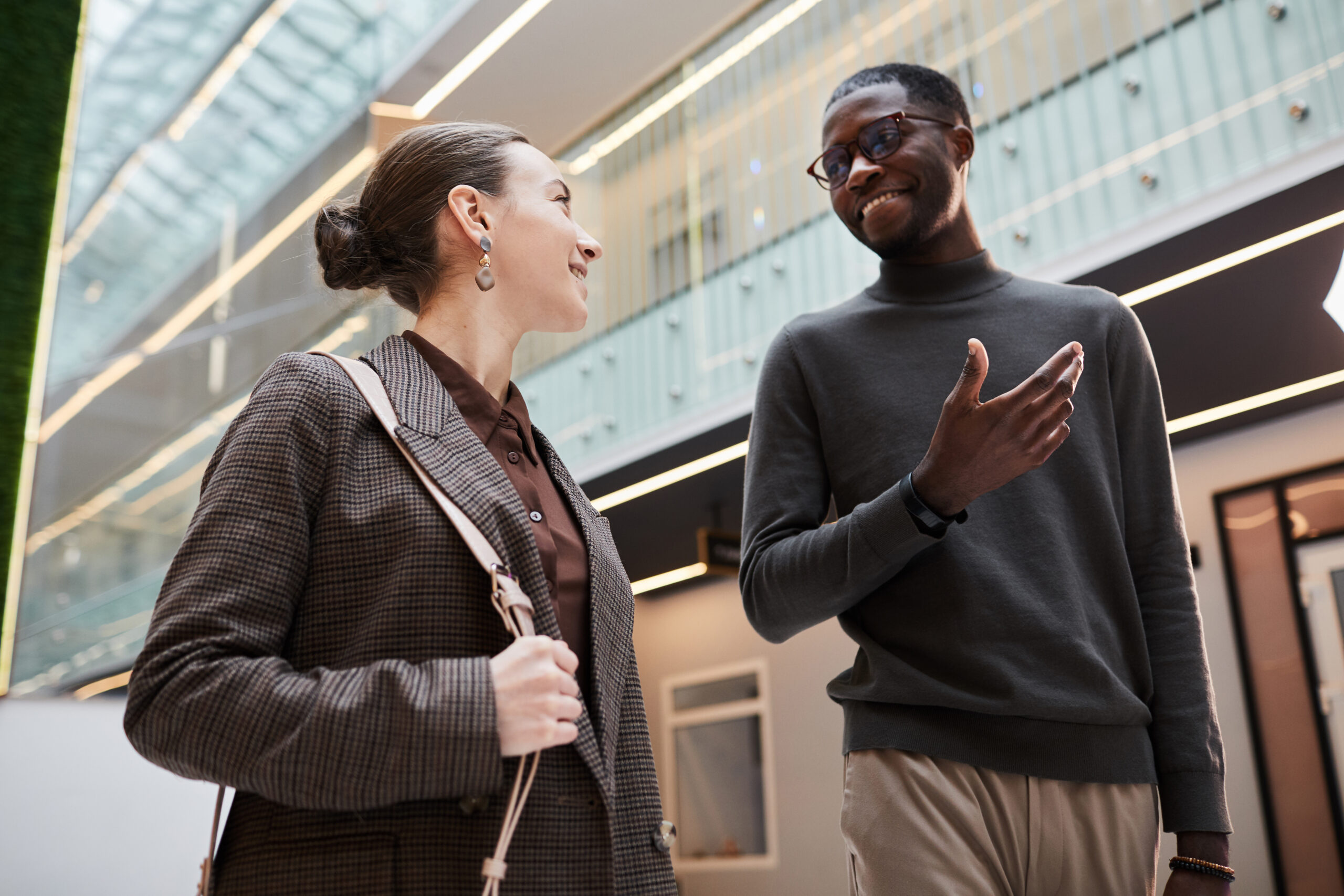 Two young professionals talking while walking in a modern office setting.